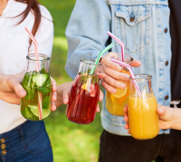 Alimentation saine. Amis buvant de la désintoxication de jus de fruits frais sur fond de nature verdoyante