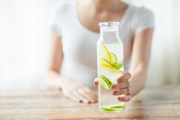 alimentation saine, boissons, alimentation, désintoxication et concept humain - gros plan d'une femme avec de l'eau de fruits dans une bouteille en verre