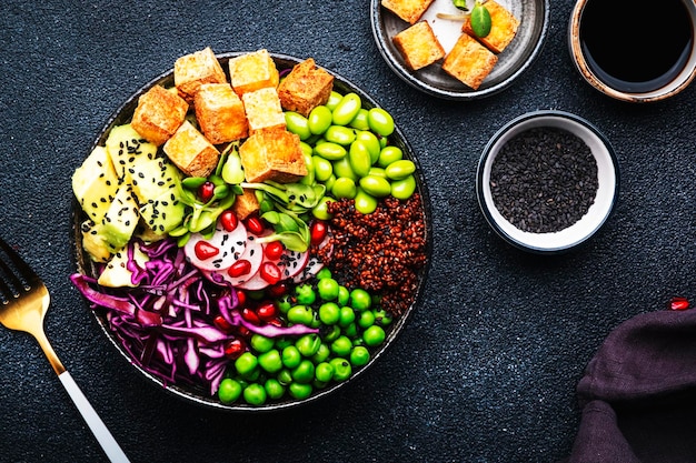 Alimentation saine bol de bouddha végétalien avec quinoa frit tofu avocat haricots edamame pois radis chou rouge et graines de sésame fond de table de cuisine noir vue de dessus