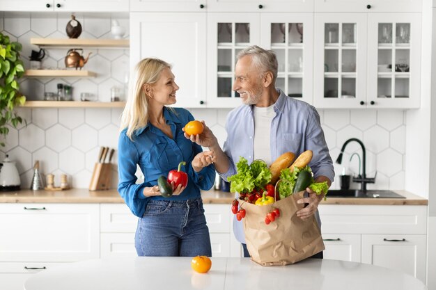 Une alimentation saine, des conjoints âgés heureux déballent des sacs en papier avec des produits d'épicerie à la maison