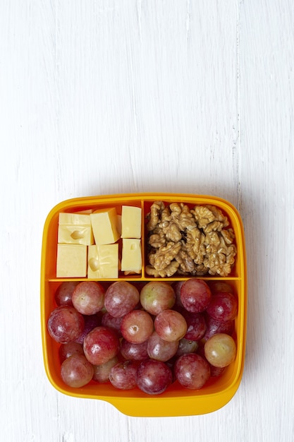 Une alimentation saine dans un récipient en plastique prêt à manger avec du fromage, des raisins et des noix sur la table