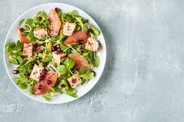 Une alimentation saine, du saumon grillé, de la roquette, du pamplemousse et de la grenade sur une table grise, vue de dessus