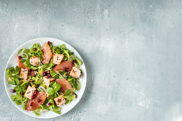 Une alimentation saine, du saumon grillé, de la roquette, du pamplemousse et de la grenade sur une table grise, vue de dessus