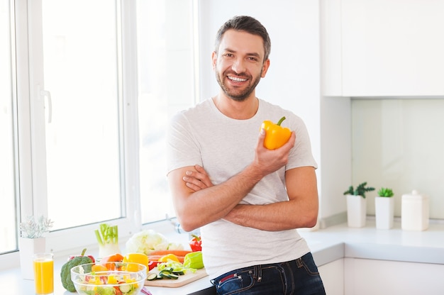 Une alimentation saine est une vie saine. Beau jeune homme tenant du poivron jaune frais et souriant en se tenant debout dans la cuisine