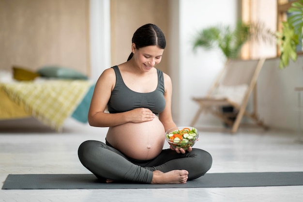 Alimentation saine Femme enceinte souriante tenant une salade de légumes frais et embrassant le ventre