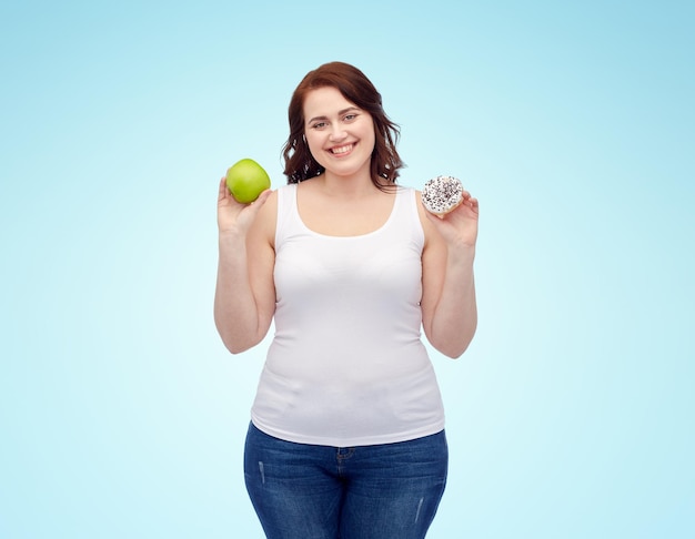 alimentation saine, malbouffe, régime alimentaire et concept de personnes de choix - femme souriante de taille plus choisissant entre pomme et biscuit sur fond bleu