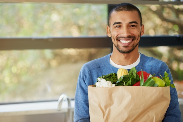 Une alimentation saine me motive à faire de mon mieux Portrait d'un jeune homme heureux tenant un sac rempli de légumes sains à la maison