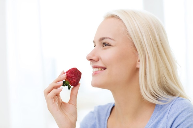 alimentation saine, nourriture, fruits, régime alimentaire et concept humain - femme heureuse mangeant des fraises à la maison