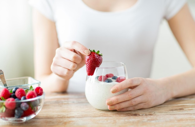 alimentation saine, nourriture végétarienne, régime alimentaire et concept de personnes - gros plan des mains de femme avec du yaourt et des baies sur la table