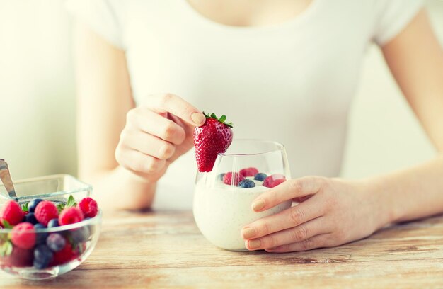 alimentation saine, nourriture végétarienne, régime alimentaire et concept de personnes - gros plan des mains de femme avec du yaourt et des baies sur la table