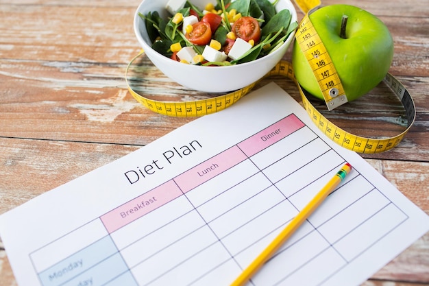 alimentation saine, régime alimentaire, perte de poids et concept de perte de poids - gros plan du plan de régime avec pomme verte, ruban à mesurer et salade
