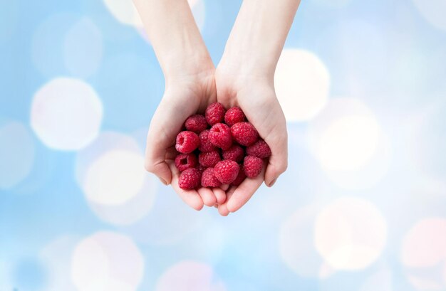 alimentation saine, régimes amaigrissants, nourriture végétarienne et concept humain - gros plan sur des mains de femme tenant des framboises mûres sur fond de lumières bleues