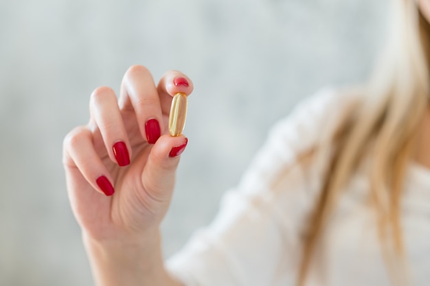 Photo une alimentation saine et des suppléments vitaminiques. femme regardant la capsule d'huile de poisson en la tenant entre les doigts.