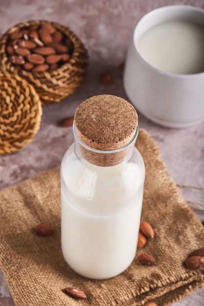 Aliments et boissons alternatifs. Lait d'amande fait maison dans une tasse et une bouteille, amandes décortiquées sur une surface rustique. Verticale