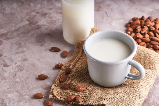 Aliments et boissons alternatifs. Lait d'amande fait maison dans une tasse et une bouteille, amandes décortiquées sur une surface rustique.