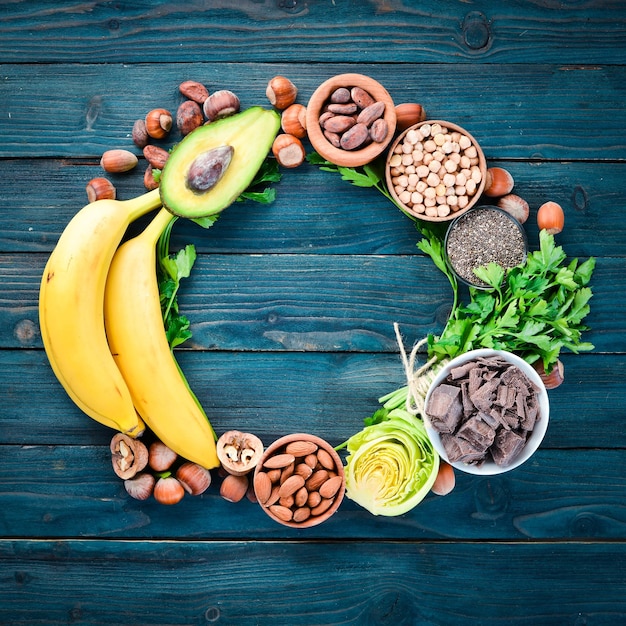 Aliments contenant du magnésium naturel Mg Chocolat Banane Noix de cacao Avocats Brocoli Amandes Vue de dessus Sur un fond de bois bleu