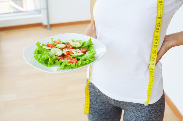 Aliments diététiques, gros plan de salade fraîche dans un bol et ruban à mesurer jaune.