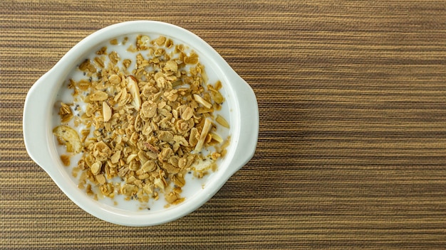 Aliments du matin en flocons et lait dans un bol blanc sur une table en bois.