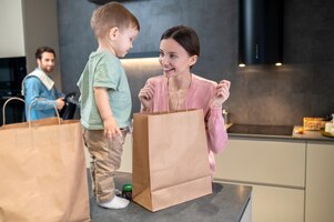 Aliments. jeune maman avec un petit enfant ouvrant des sacs avec de la nourriture dans la cuisine
