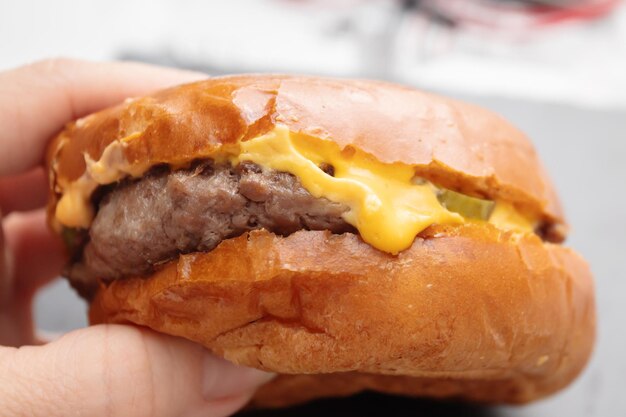 Aliments non diététiques gras nocifs. La main tient un hamburger avec une escalope de viande, du fromage, des concombres marinés