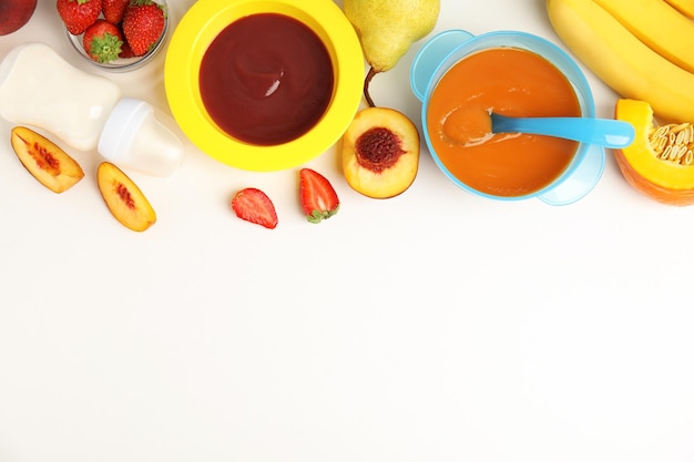 Aliments pour bébés dans des bols et des ingrédients frais sur une table blanche à plat Espace pour le texte