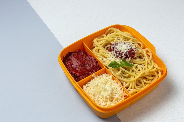 Des aliments sains dans des contenants en plastique prêts à manger avec des spaghettis faits maison avec tomate, fromage et basilic sur la table de travail. Nourriture italienne. À emporter.