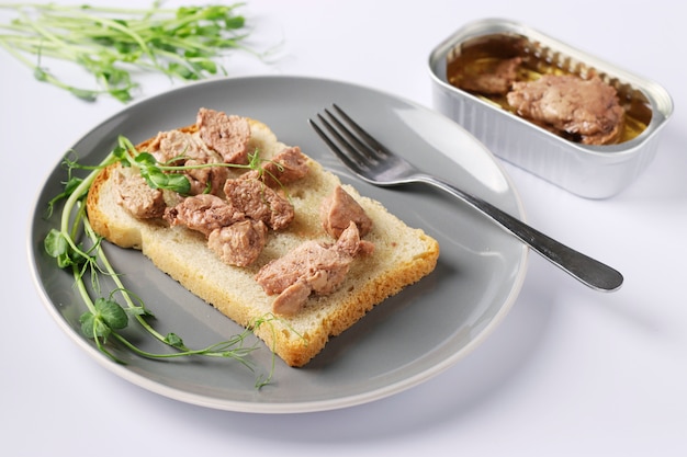 Des aliments sains, un sandwich au foie de morue et des microgrines de pois sur une plaque grise sur fond blanc