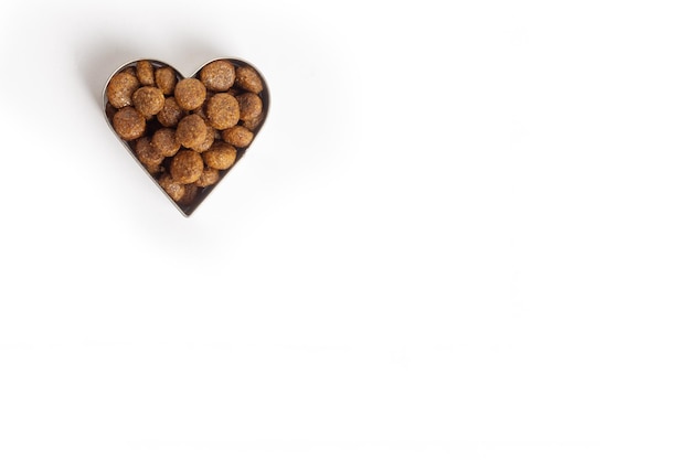 Les aliments secs pour animaux de compagnie en forme de coeur sont isolés sur fond blanc Pellets d'aliments sains pour chiens et chats