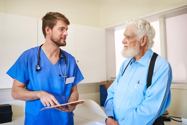 Allez au fond de votre douleur Photo d'un jeune médecin et de son patient âgé discutant ensemble de son dossier médical