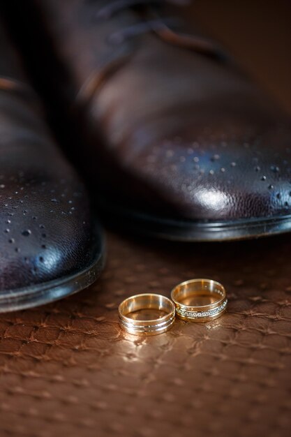 Les alliances en or des jeunes mariés se trouvent à côté des chaussures pour hommes pour le marié