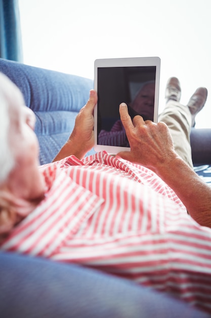 Allongé sur un canapé senior man touching digital tablet