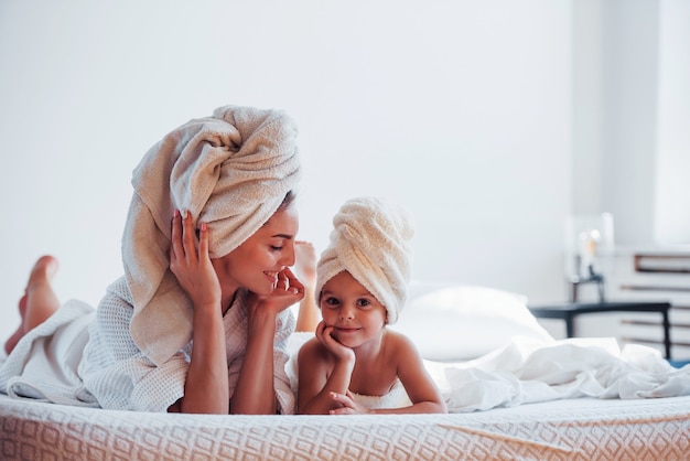 Allongé sur un lit blanc ensemble. Une jeune mère avec sa fille a une journée de beauté à l'intérieur dans la chambre.