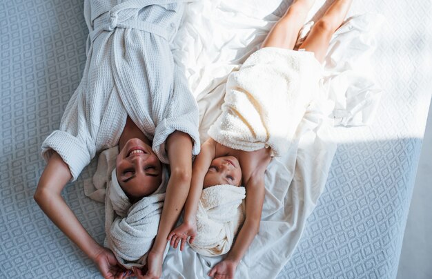 Allongé sur le lit. Une jeune mère avec sa fille a une journée de beauté à l'intérieur dans une salle blanche.