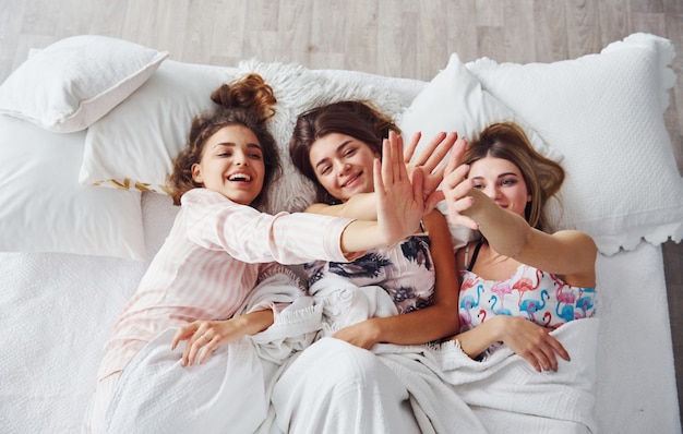 Allongé sur le lit sous la couverture ensemble. Joyeuses amies s'amusant à une soirée pyjama dans la chambre.