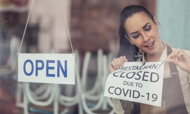 Alors que les restrictions de Covid19 facilitent le propriétaire du restaurant, il décolle le panneau de fermeture en plaçant un panneau ouvert sur une fenêtre