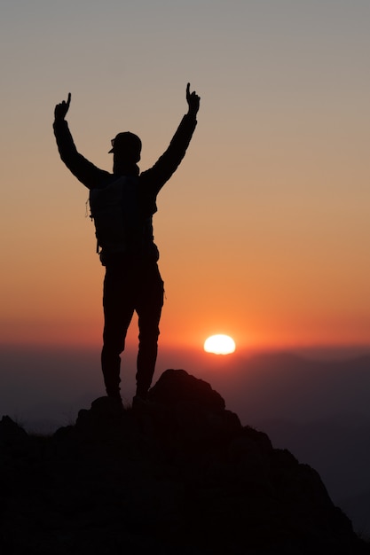 L'alpiniste conquiert le sommet au coucher du soleil. En silhouette