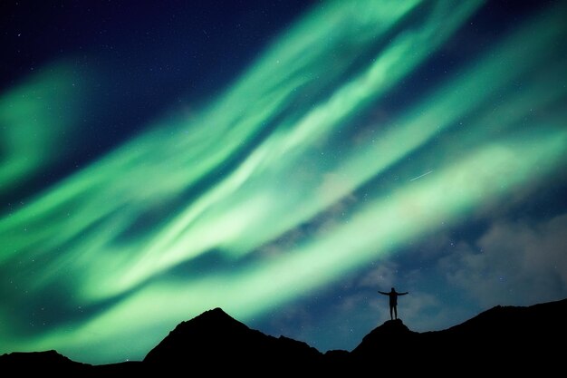 Alpiniste debout au sommet de la montagne avec une aurore boréale qui brille dans le ciel nocturne sur le cercle arctique