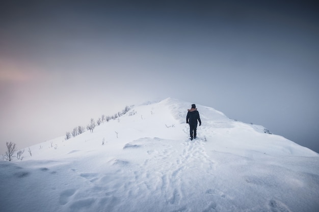 Alpiniste homme marchant sur la crête de la montagne enneigée avec blizzard par temps sombre à l'île de Senja