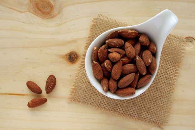 Amandes dans un bol blanc avec tissu de sac sur la table en bois