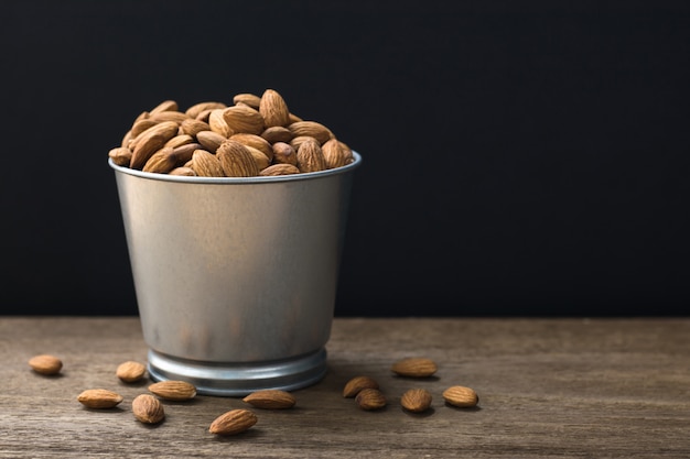 Photo amandes dans un seau stanless sur une table en bois avec espace copie. fond noir