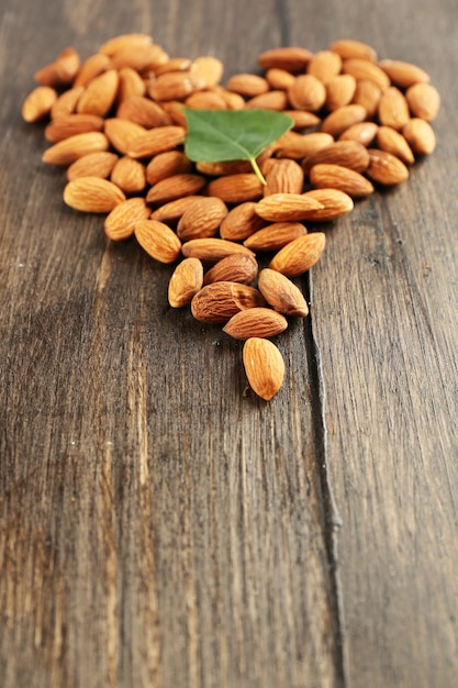 Amandes disposées en forme de coeur avec feuille verte sur fond de bois