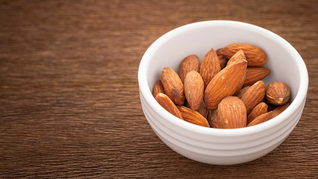 Amandes salées grillées dans un bol en céramique simplement blanc sur fond de texture de bois naturel rustique, rapport Full HD