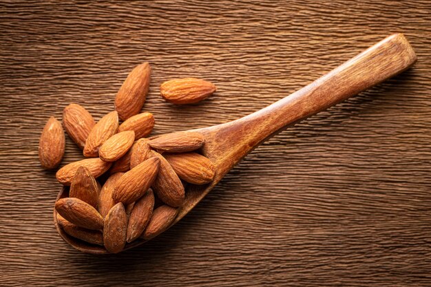 Amandes salées grillées dans une cuillère en bois sur fond de texture de bois naturel rustique, ton brun d'harmonie