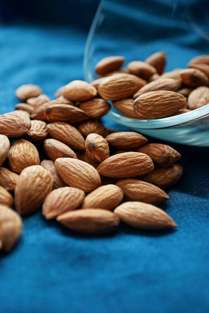 Les amandes sèches sont dispersées dans un bol sur une surface bleue.