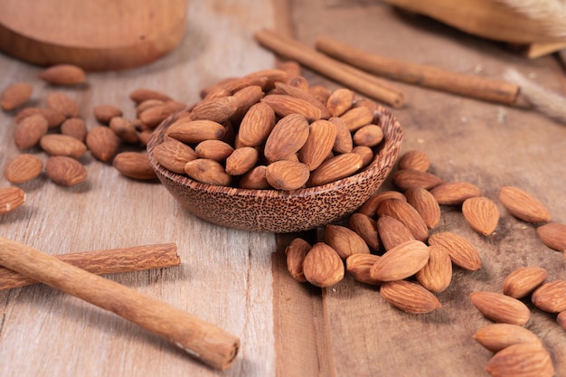 Amandes servies dans un petit bol en bois avec des amandes éparpillées et des cannelles sur le côté