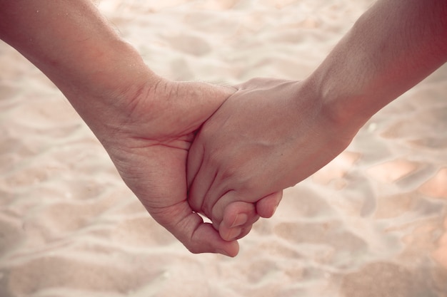 amant tenir la main sur la plage avec une vague de sable, style vintage