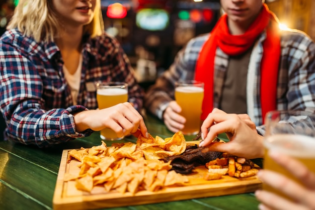 Les amateurs de football boivent de la bière et mangent des chips à la table du bar des sports.