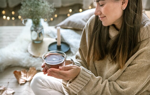 Ambiance chaleureuse à la maison d'automne, une femme avec une tasse de thé dans ses mains. Le concept de repos et de confort.