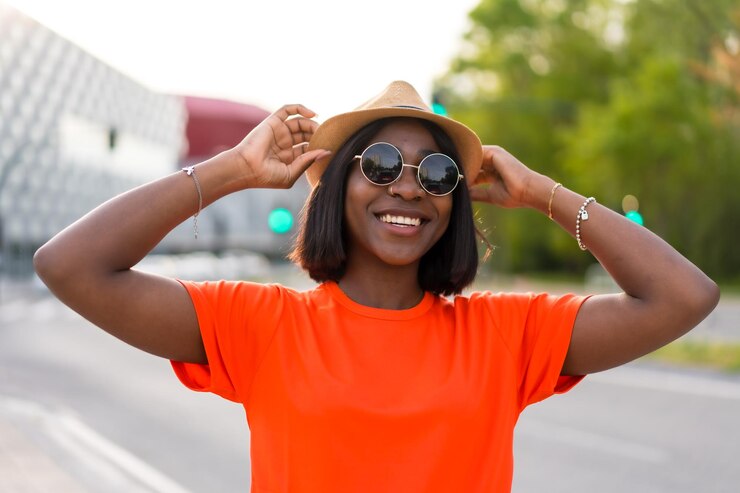 Ambiance estivale Jeune femme noire touriste en t-shirt vert et lunettes de soleil contre des photos de style de vie de mur brun