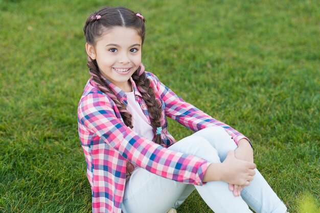 Ambiance estivale petite fille se détendre sur l'herbe verte Parcs et plein air Nature printanière Pique-nique d'été Petite écolière aux cheveux à la mode enfance heureuse parc avec herbe verte assis sur l'herbe verte